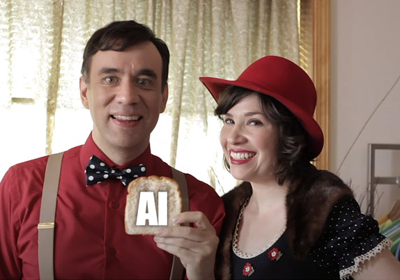 Fred Armisen and Carrie Brownstein in the classic Put A Bird On It sketch from Portlandia. They are holding a piece of toast, but instead of there being a bird on it, there are the letters AI.