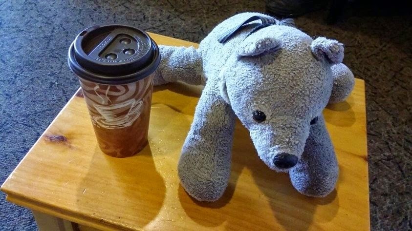 The world's cutest stuffed wolf next to a cup of coffee.