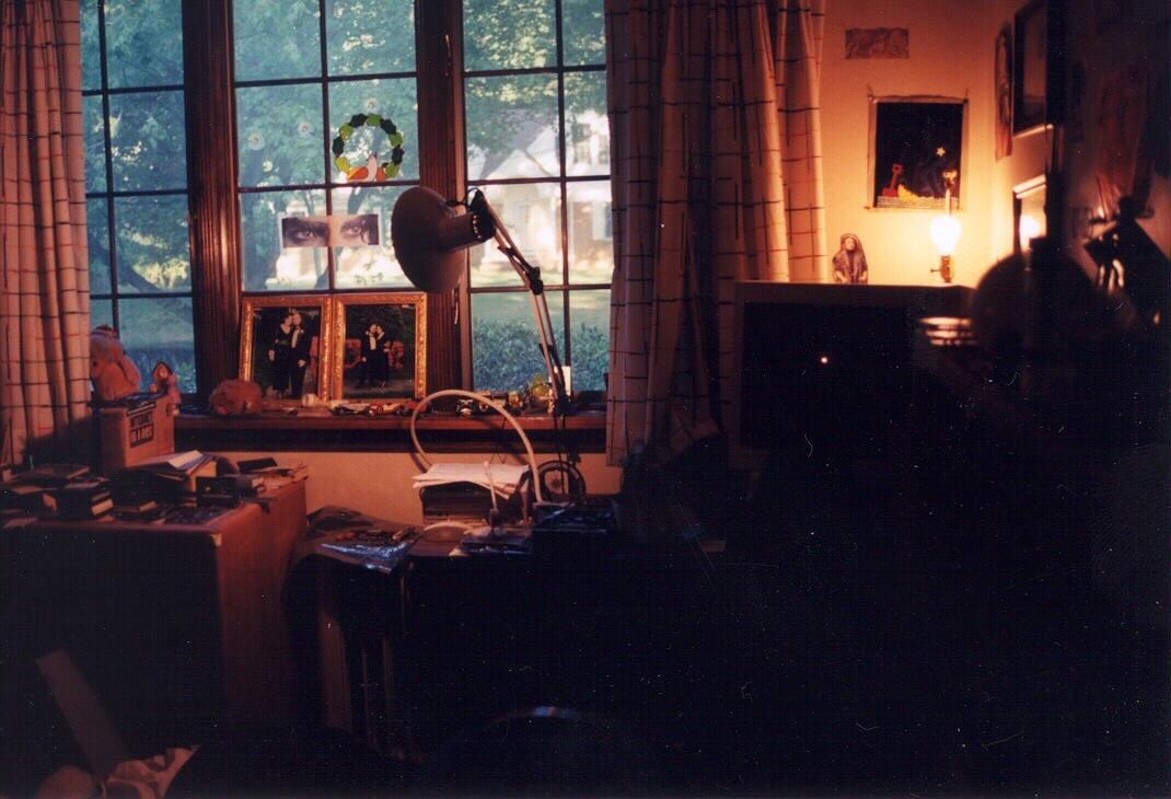 Another corner of that bedroom. Still too much stuff. It’s hard to see because the foreground is entirely in shadow because I thought I was being artsy when taking the photo (although I would certainly not have said that at the time) and there’s an exposed lightbulb in s lamp behind a computer monitor. There are various things cut out of magazines taped to various windows and walls. It’s a terrible mess all around. 