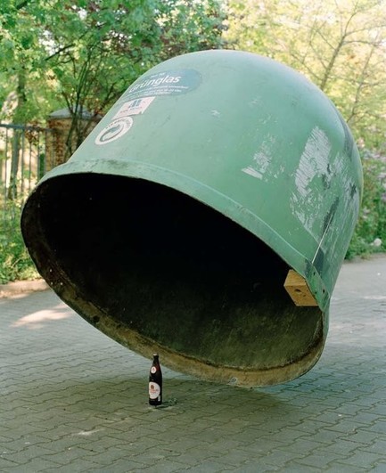 A large green metal container angled above a bottle of beer.