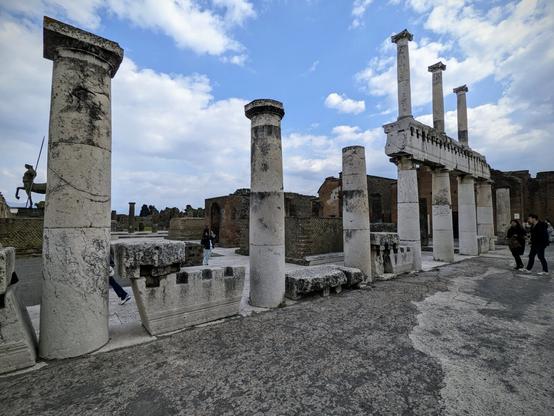 In the lower right-hand corner, there is a clear area made of dark grey stone.  Going from the lower left-hand corner to the upper right-hand corner, there are foundational pillars.  The most distant pillars are topped with a horizontal stone, followed by another level.  A pegasus statue is visible in the distance.