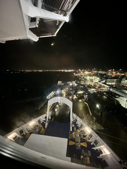 Wide angle view forward from a cabin at the front of deck 11 on the Stena Hollandica, overlooking the bow on a dark night. The bow is open to load vehicles, streetlights are visible on the horizon, and the underside of the bridge is visible at the top.