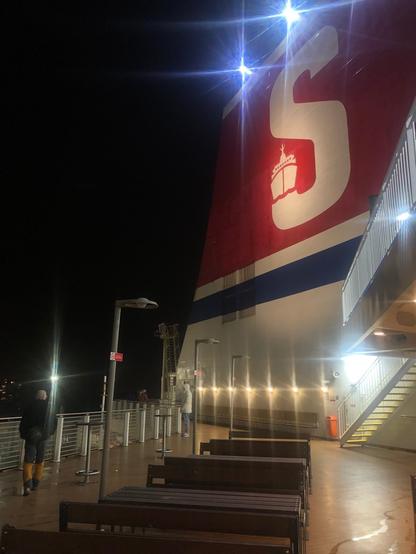 View of the stern of the ferry, as seen from the deck, in the dark. The Stena Line logo is very prominent. It's a white letter S on a red background, with a picture of a boat on the lower-left end of the S.