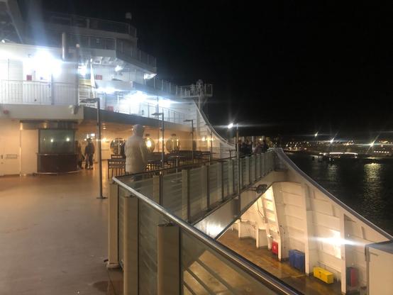 View of the deck of the Stena Line boat. A few people are standing huddled together. It's dark, but this deck and the other decks are brightly lit.