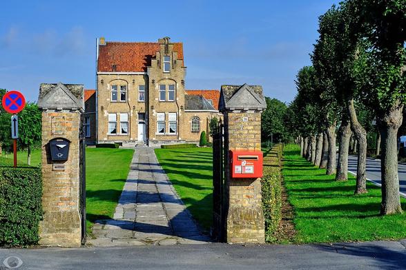The #Eksternest is a youth house where children provide for their own needs. It's housed in an early 20th century yellow brick building in a stair roof style that is typical for the area around Ypres. Lined to the right with a hedge and trees. The entrance has a flaming red mailbox.