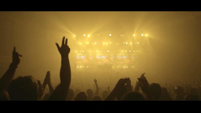 Amidst yellow foggy lighting, the audience dances with delight at a music concert by Underworld in the huge concert hall of the Sydney Opera House.