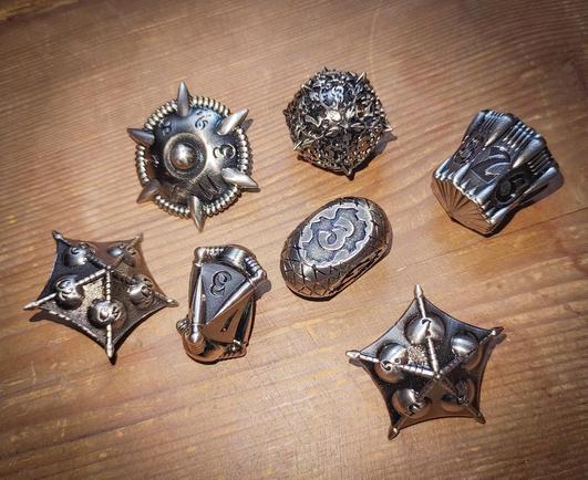 Foto von einem Würfelset bestehend aus sieben silberfarbenen Metallwürfeln, die unterschiedliche Formen haben und sehr ungewöhnlich aussehen.