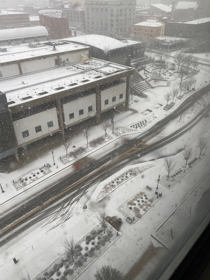 Color image of new rain, sleet, freezing rain and snow falling on a downtown street, Akron, Summit County, Ohio, USA. Image shows a snow-covered main street passing through a city, adjacent buildings covered in new snow, street marked with the tracks of vehicles.