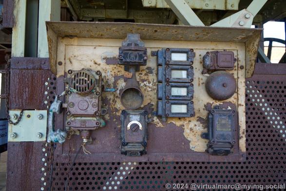 A photo of an old signalling machine and mine telephone at the bottom of a winding tower. Everything is rusty and corroded.