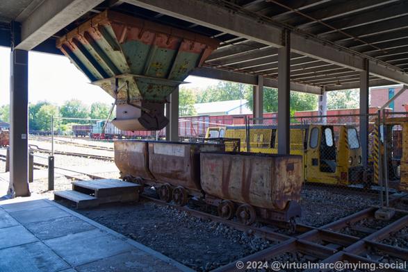 A photo of the bottom of the mine hall bellow the winding tower. You can see minecarts on rails bellow a coal filling station.