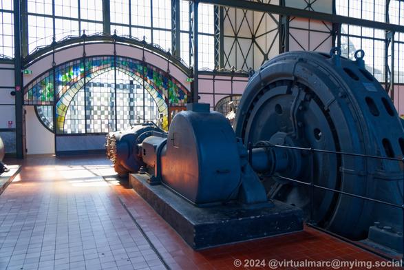 A photo of a blue generator in front of the art nouveau entrance portal inside the machine hall.