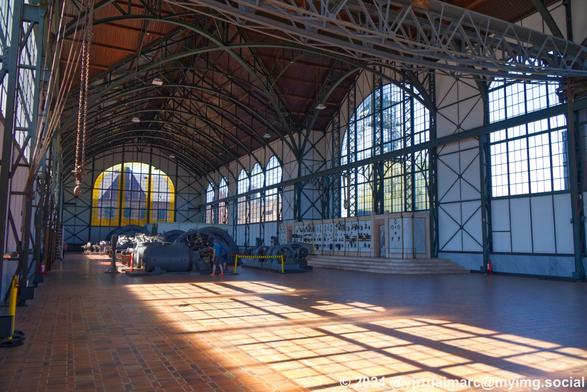 A photo of the inside of the machine hall. The machines and the marmor wall with the scales, buttons and levers can be seen. Part of the ceiling crane can also be seen. There are big windows all around.