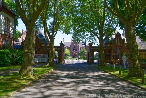 A photo of an avenue towards the main entrance buildings and gates of Zeche Zollern. There are Trees on both sides. You can see the administrative building behind the entrance gate.
