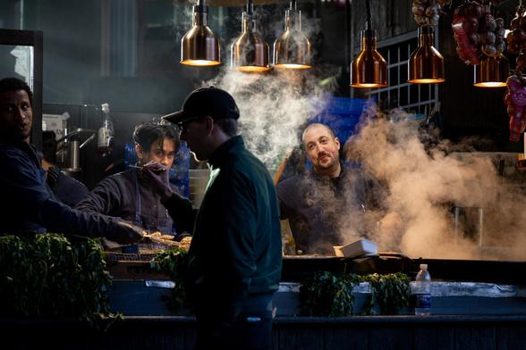 Shot of a stall selling risotto. A chef is stirring the food in a big pan, steam is rising off of it and his face is framed by the steam.