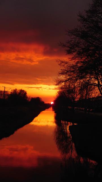 Zonsondergang boven een sloot. De hemel is rood/Oranje geschakeerd. De hemelkleuren worden weerspiegeld in de sloot