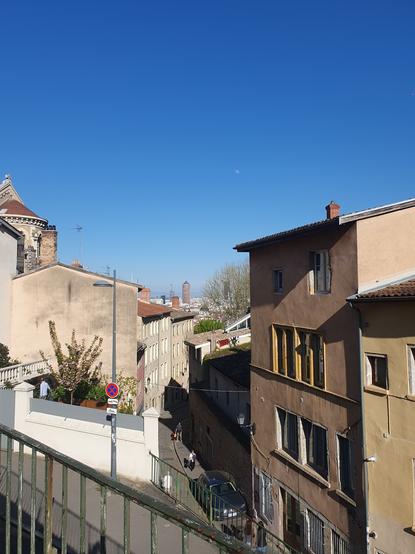 top of Montée du Gourguillon, one of the many climb toward Fourvière. surrounded by buildings, with some pedestrians finishing their climb. at horizon we see the towers of La Part Dieu, under a blue shiny sky