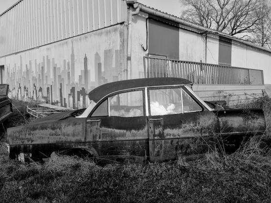 A rusty old car abandoned near a hanger
