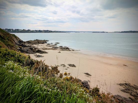 La côte avec l'océan, une plage, des rochers et un chemin herbeux. Le ciel est orageux mais encore beau.