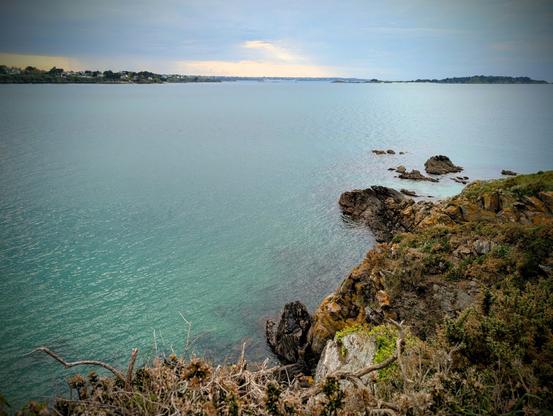 La côte avec l'océan couleur émeraude et des rochers. Le ciel est orageux mais encore beau.