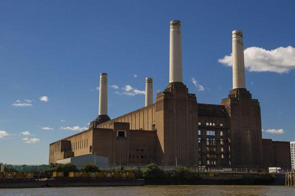 a photo of the power station, it is a simple and powerful design, it is a reddish brown  large building with four giant white smoke stacks, a blue sky behind it with clouds in it
