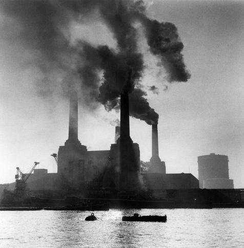 a photo of the station from the river when it was active, smoke coming out of the tall smoke stacks