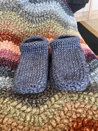 A heathered blue pair of gammlo’s / slippers on top of a rainbow wave blanket