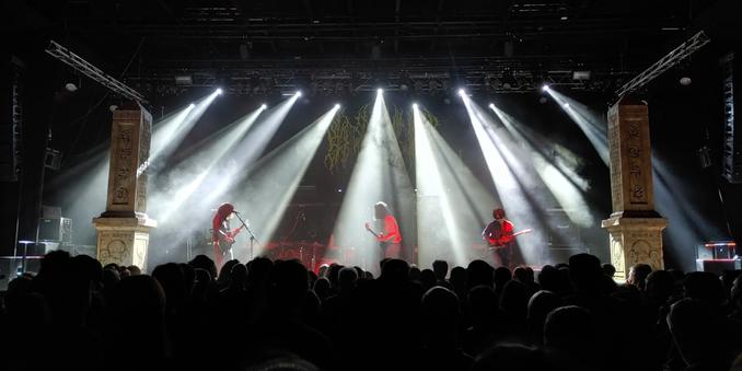 muzycy na scenie wśród snopów świateł, po bokach sceny dwa obeliski
