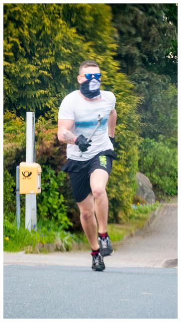 Neonazi Nordulf Heise rennt mit einem 60cm großen Schraubenschlüssel, mit einem Schlauchschal der 'Arischen Bruderschaft' und Sonnenbrille vermummt hinter dem Auto der Journalisten her. 
Das Bild ist aus diesem Auto in der Rückwärtsfahrt aufgenommen worden. 
Um das Hochkantbild ist ein kleiner weißer Rahmen