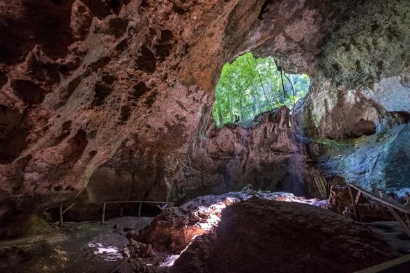 A large cave with jagged rock formations and a clear opening at the top, allowing sunlight to illuminate the interior.