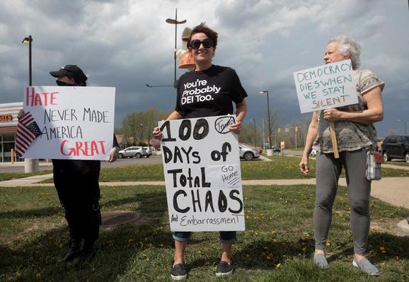 Protesters hold placards reading:
"100 days of total chaos and embarrassment"
"Hate never made America great"
#Democracy dies when we stay silent"