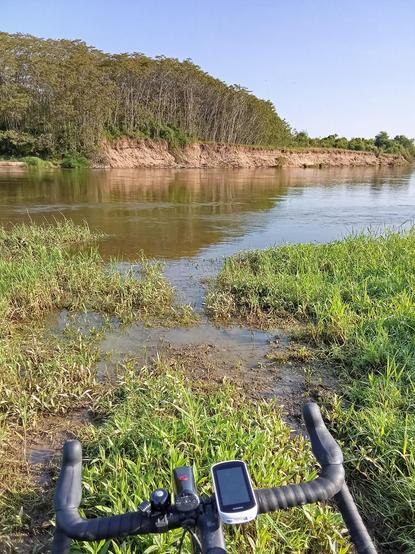 We can see a gravelbike's handlebar. The bike is standing in front of a large river.