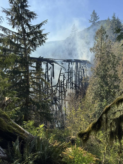 Photo showing the moment the first few spans of the charred wooden trestle collapsed.