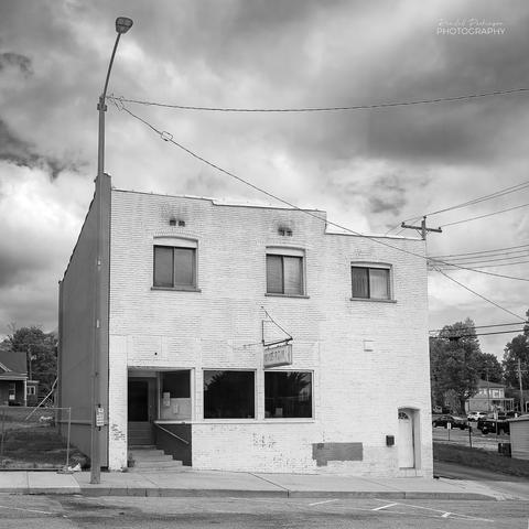 A two story brick building painted white.  There are three windows on the upper level.  The lower level has a door and two windows for a pizza restaurant and a separate door for the upstairs apartment.