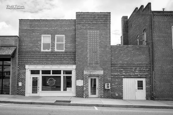 The front of a two story brick building housing a youth crisis counseling service.  The center portion of the building has an entry door with the words "CITY HALL" in stone above the door.  Above that is a large, vertical glass block window.
