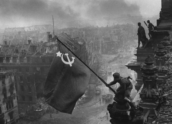 Sowjetsoldat hisst 1945 russische Flagge auf dem Reichstag. Im Hintergrund das zerbombte Berlin.