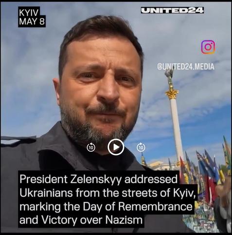 A screen capture from the video shows Zelenskyy looking toward the camera with his face a little pursed as he gathers his thoughts and clears his throat. In the background you can see the tall monument that stands in the centre of Kyiv is surrounded by flags.