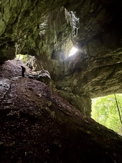 Person descends through cave, lit by natural windows & entrance