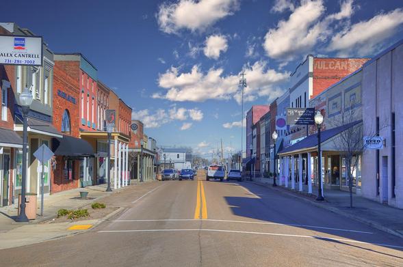 A lively street scene showcases a small town's main road lined with colorful brick buildings under a bright blue sky.
