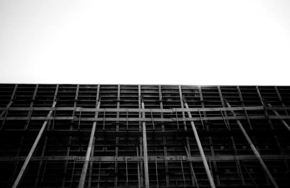 Black and white picture of a big metal wall with large pillars, blocking the sunlight