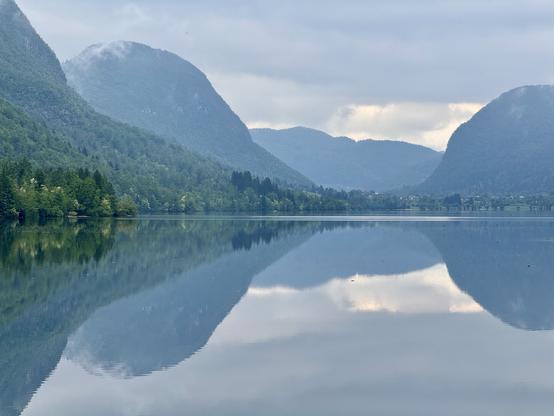 Mountains reflected in still lake surface on overcast day. 

Bohinjsko jezero | Lake Bohinj is 45m deep, 4.2km long & 1.2km wide. Its water is fully exchanged 3 times per year.