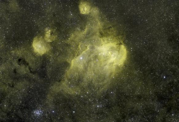 A large bright nebula surrounded by dark dust and smaller nebulosity. If you squint just so, it can vaguely look like a chicken running at you. A bright star cluster sits at bottom left.  Silhouetted against the bright center of the nebula are tiny black cocoons of dust. All of this sits on a dense field of stars.