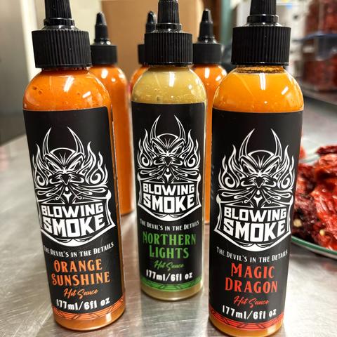 Three bottles of Blowing Smoke hot sauce: Orange Sunshine, Northern Lights, Magic Dragon.