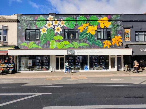 A wide estate agents with upper story mural of yellow tropical flowers and greenery against grey background.