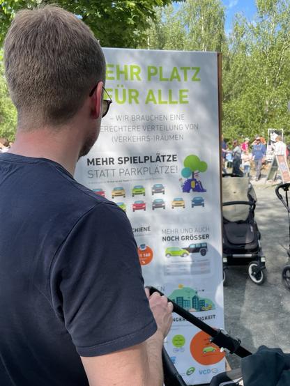 Im Vordergrund ist ein Mann von hinten fotografiert, der sich ein Infomationsschild durchliest. Die Überschrift von dem Informationsschild ist "Mehr Platz für alle - Wir brauchen eine gerechtere Verteilung von (Verkehrs-)Räumen".