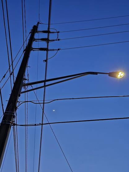 Street lamp and electrical pole with power lines making tic tac toe squares against the dark blue sky.