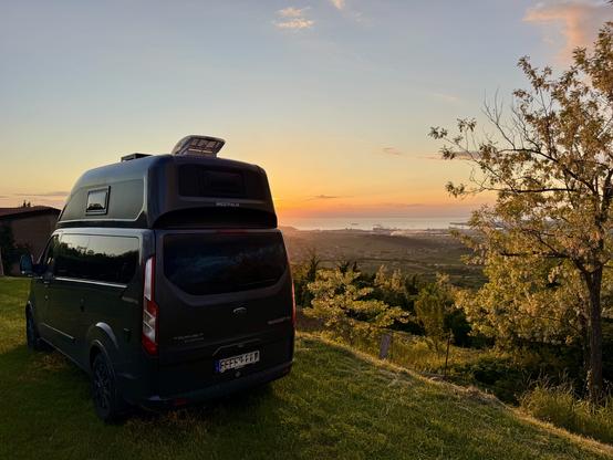 Camper van on grass pitch at sunset, with view to Adriatic port town