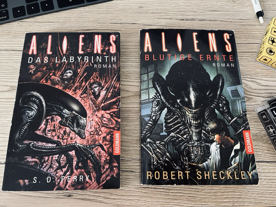 Two books on a table. The first: "Aliens - Das Labyrinth", by S.D. Perry. The second "Aliens - Blutige Ernte", by Robert Sheckley.