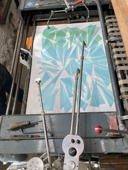 Plakatdruck auf einer Druckpresse. Zweite Druckgang. Formen wie Glassplittern gedruckt in verschiedene Blau-Grün Töne.