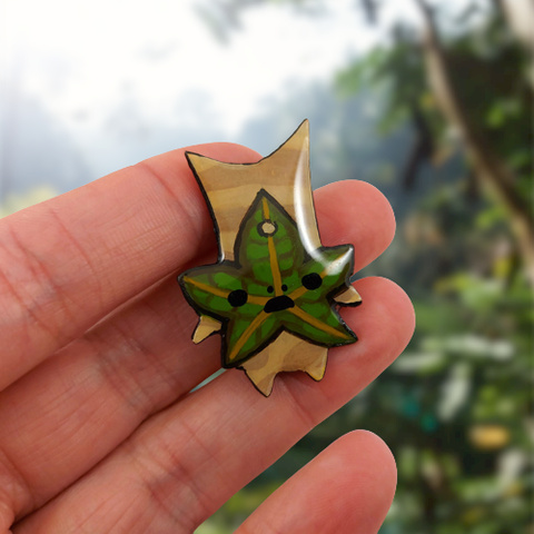 Magnet éco-responsable en forme de Korogu (issu de l'univers du jeu vidéo Zelda).
La perle est réalisée en CD recyclé, découpée et peinte à la main, puis recouverte de résine époxy.