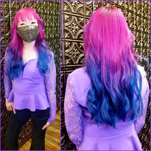 A composite shot shows a front and back portrait of me. Standing centered against a decorated wall with gold-toned decorative tiles, framed in purple. The left panel me facing the camera with a sequined black mask on, the right panel has back view of head and shoulders. I have vivid pink and blue ombre hair, a lavender lace and peplum top, and black trousers. Shot in portrait orientation with strong lighting to accentuate the hair's color gradient.